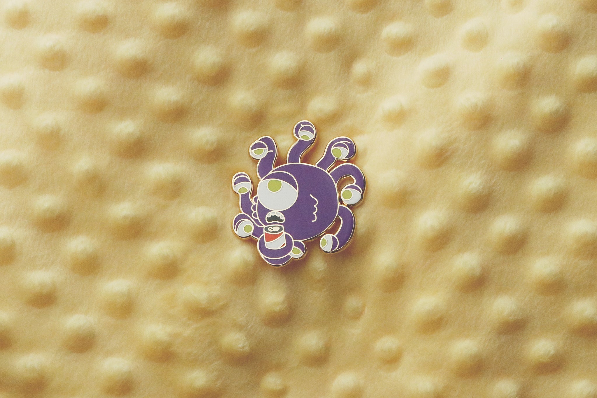 Gold plated hard enamel pin of a beholder holding a beer can.