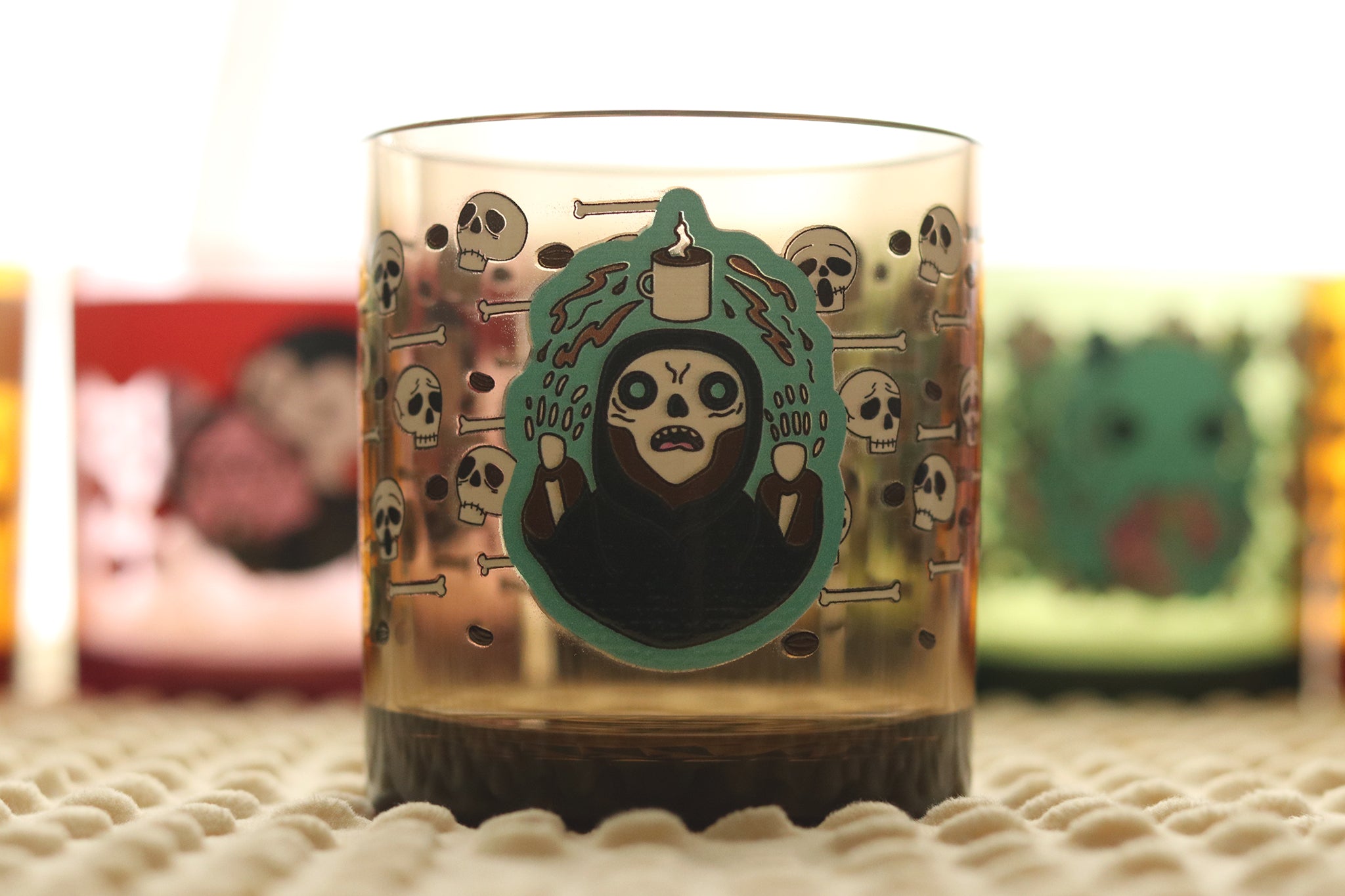 Drinking cup featuring a necromancer lich character with glowing eyes summoning a cup of coffee and surrounded by skulls and crossbones in a repeating pattern around the cup.