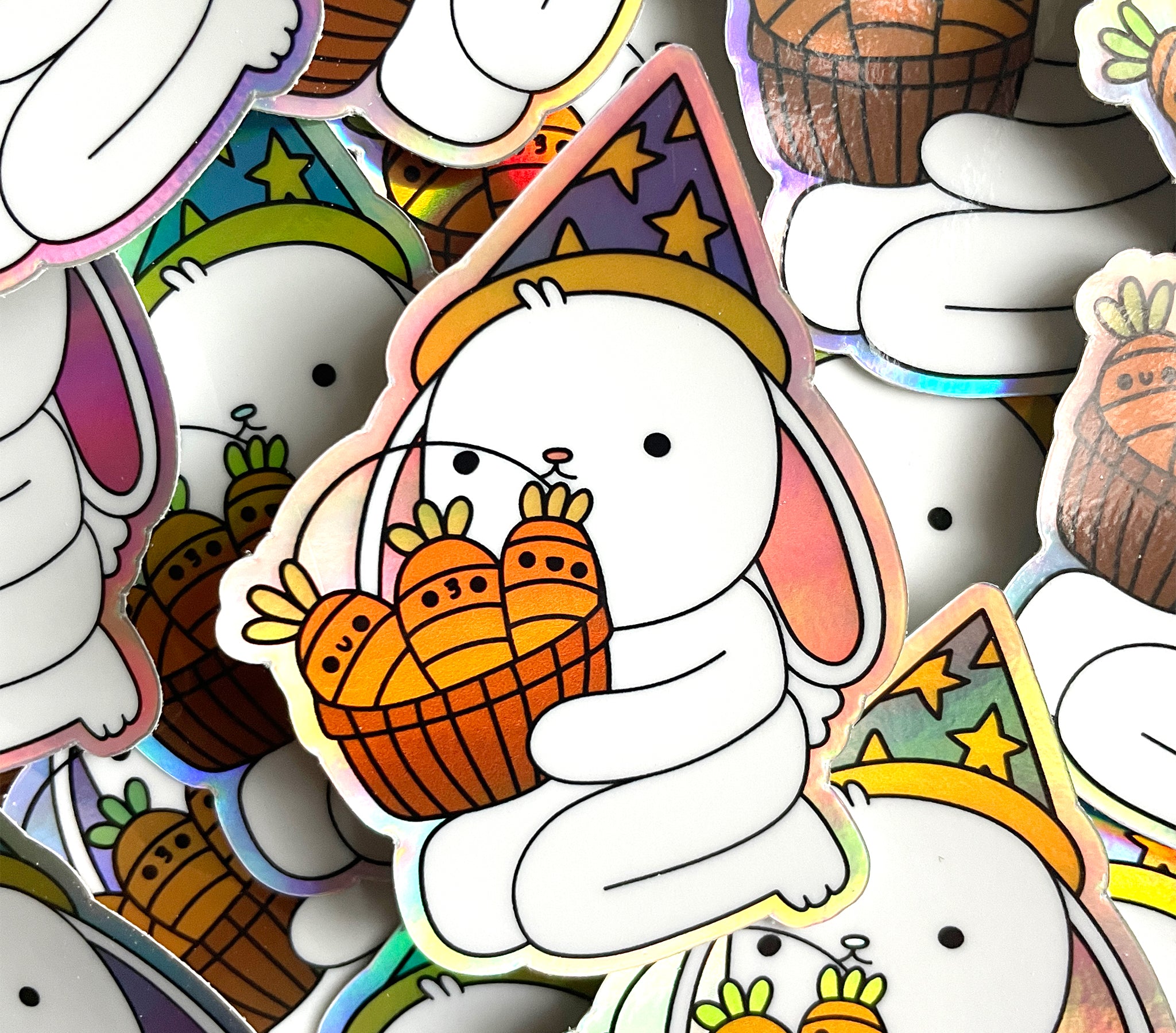 Pile of rainbow holographic stickers picturing a white lop-eared bunny wearing a blue wizard hat and carrying a basket of cute carrots.