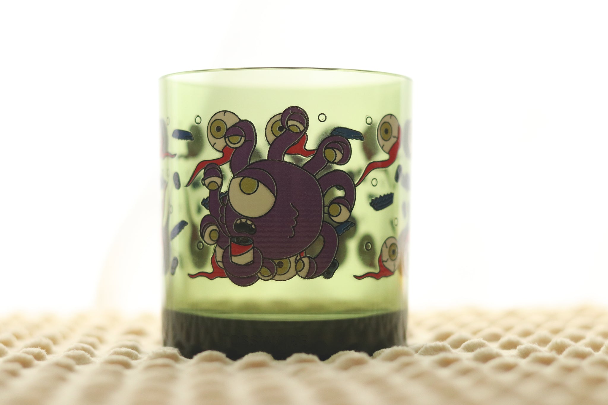Close-up view of the Beholder Beer Holder drinking glass showing detailed artwork of Dungeons & Dragons beholder creature with eyestalks gripping a beer can.