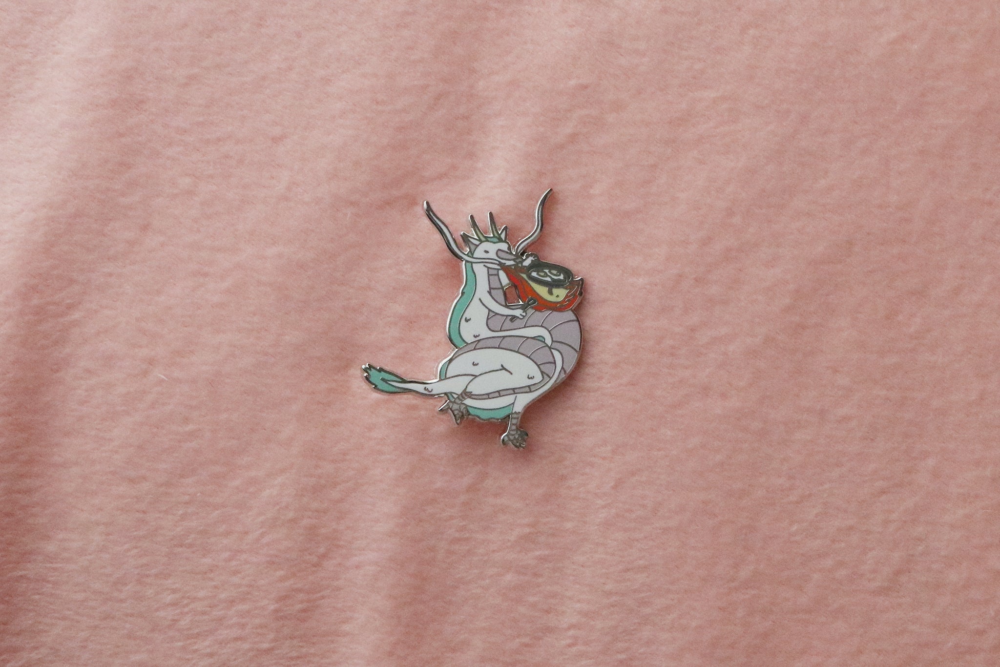 a hard enamel silver-plated pin of a  dragon using their natural fire-breathing ability for something as mundane as frying eggs for breakfast!