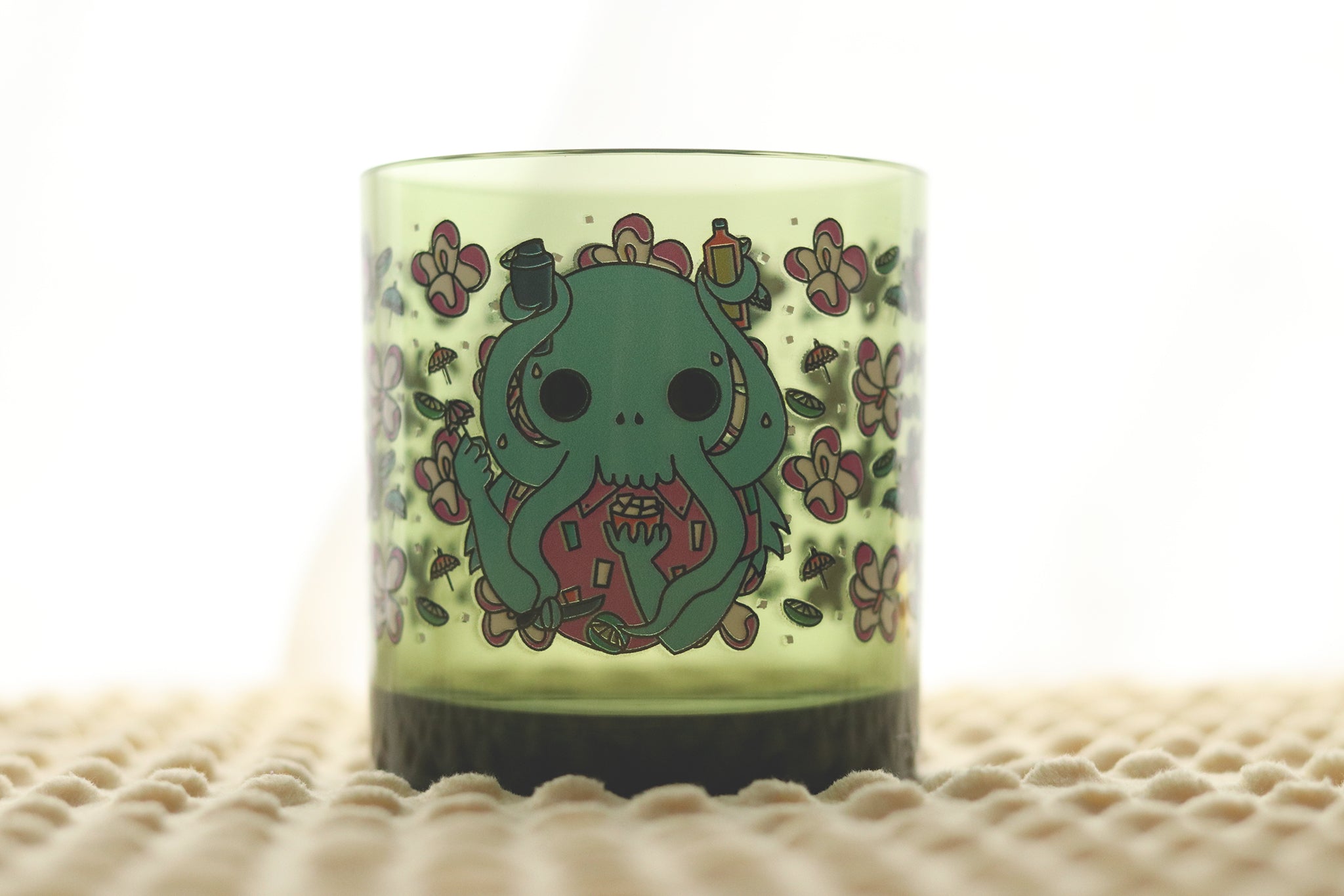 Cthulhu Tiki Tossware glass features the tentacle monster creating tiki cocktails, surrounded by tropical flowers and tiki elements on a lime green plastic glass.