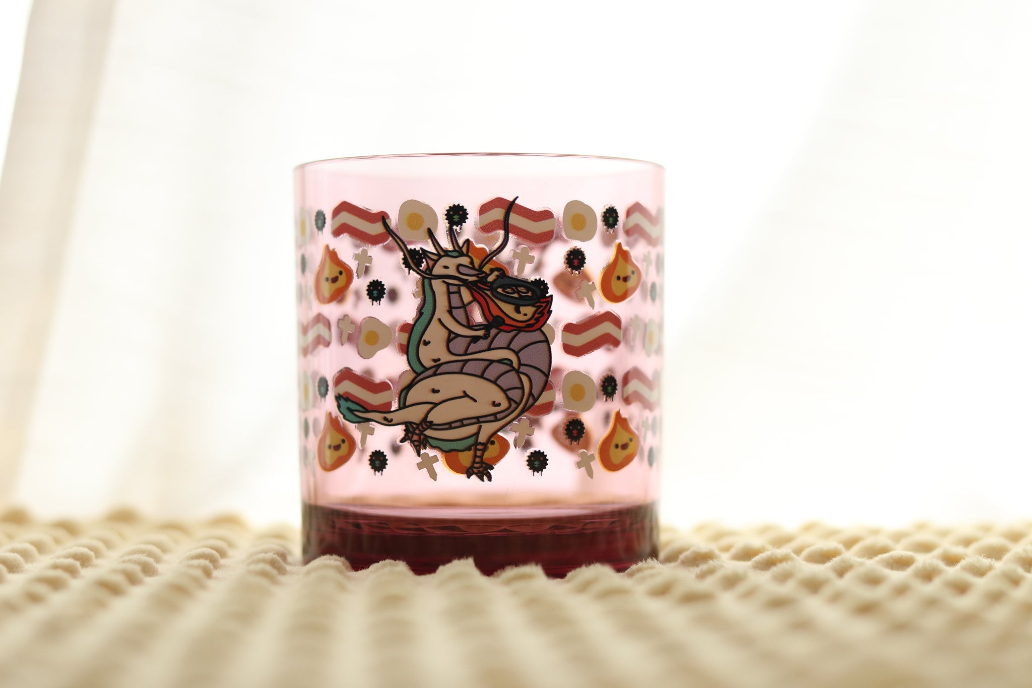 Close-up view of Dragon's Breakfast reusable drinking glass showing detailed artwork of cartoon dragon cooking breakfast eggs in a skillet. Bacon, Eggs, Fire, Soot Sprites, and Paper Shikigami in reference to classic anime films.