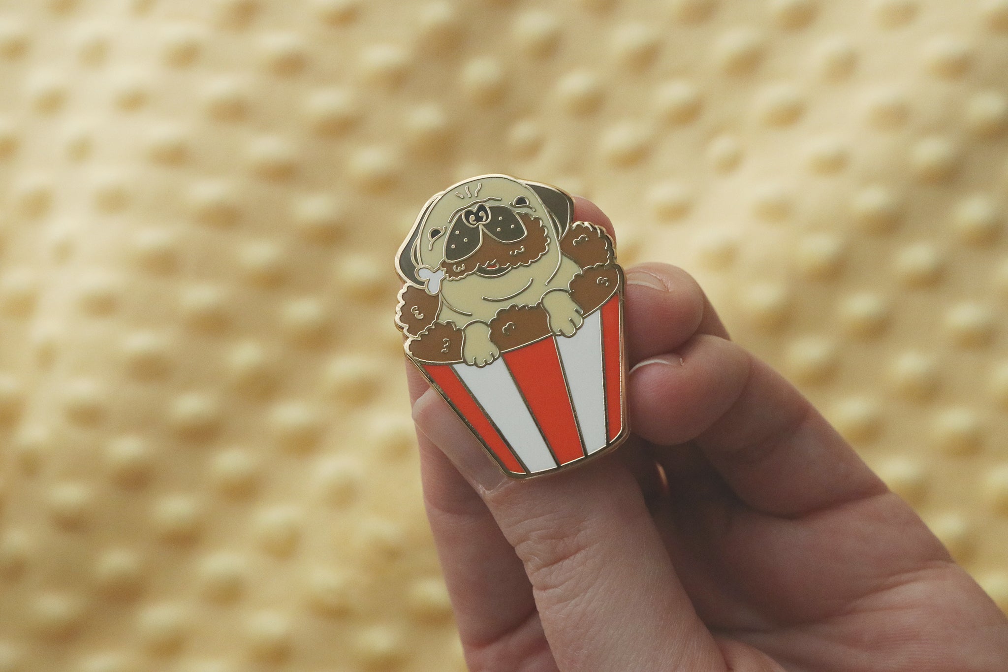 Enamel pin depicting a cute pug dog with its paws hanging over the edge of a red and white striped fried chicken bucket.