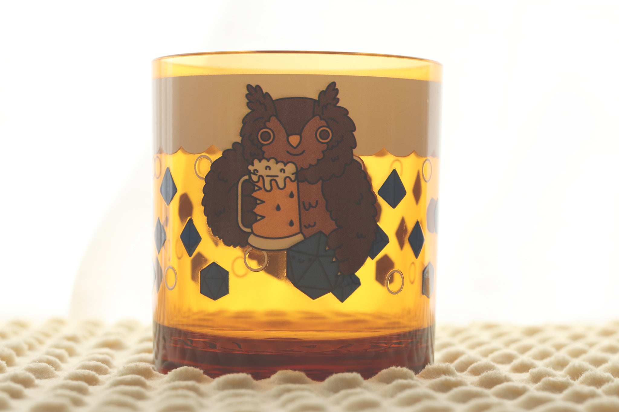 Amber-colored drinking cup featuring a cartoon owlbear character holding a beer mug, surrounded by polyhedral dice and bubbles.
