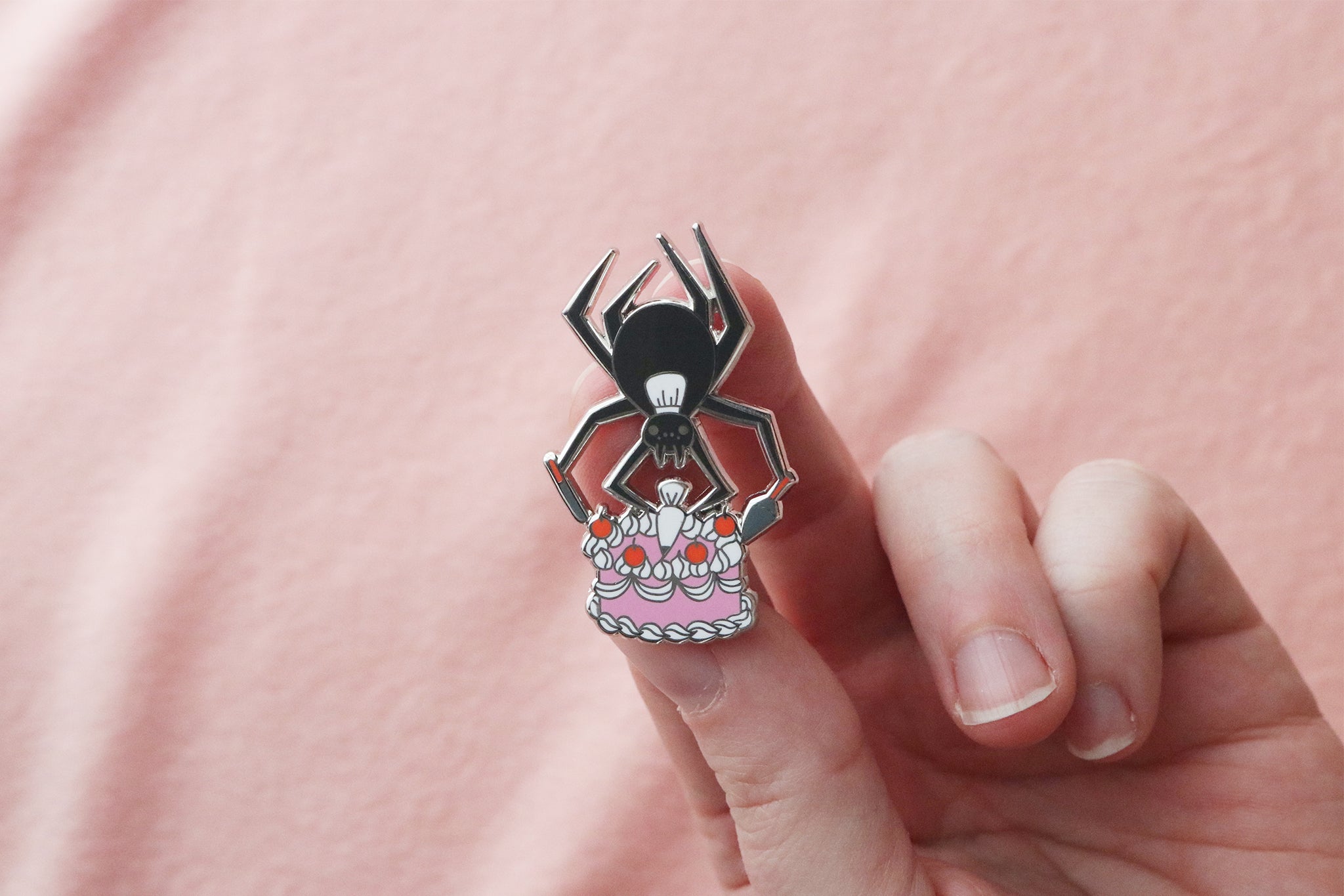 Spider pastry chef enamel pin held in hand showing detailed cake decorating scene