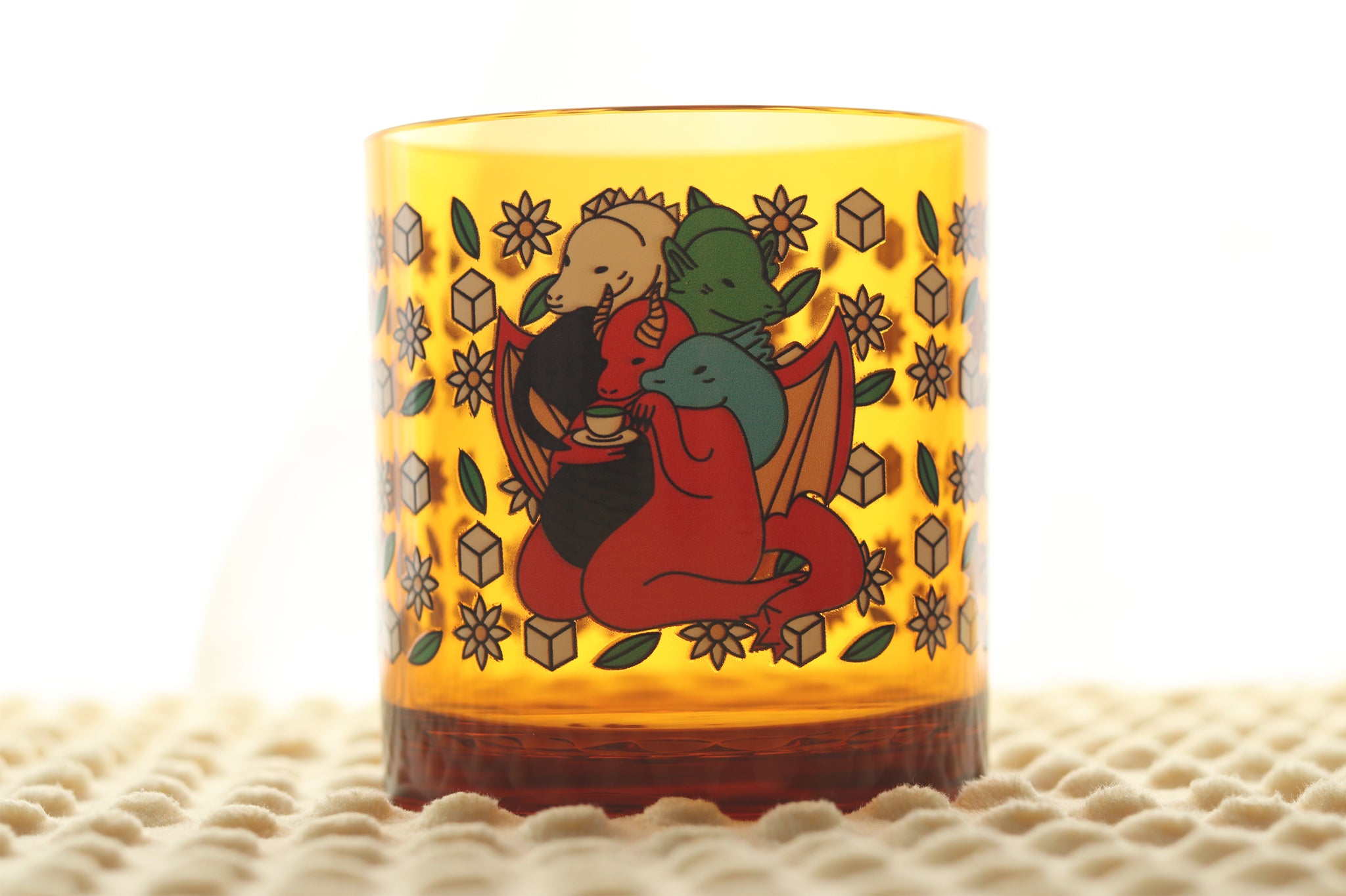 Amber plastic drinking cup displaying Tiamat drinking a cup of matcha surrounded by decorative flowers, tea leaves, and sugar cubes.