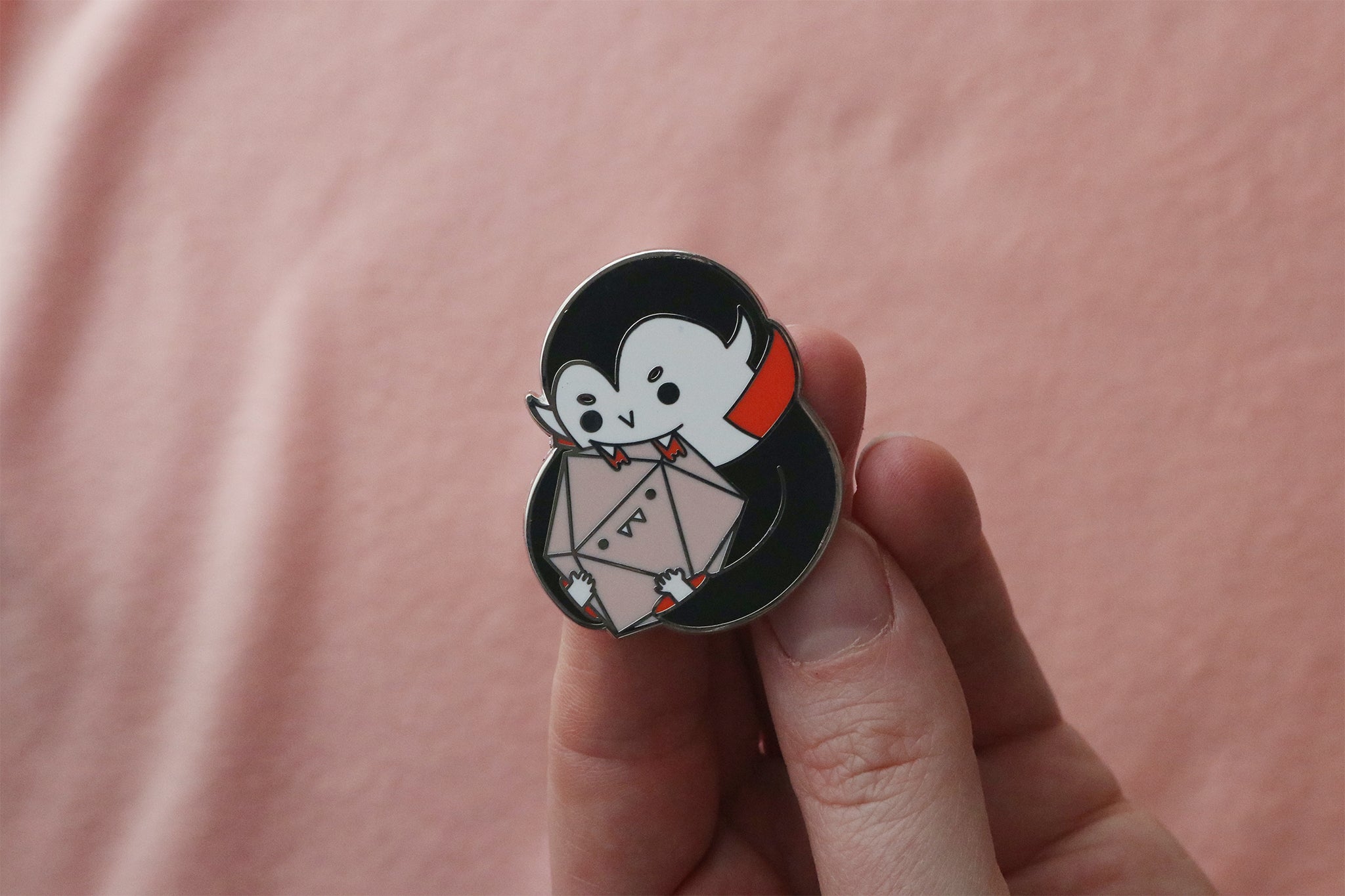 Vampire D20 enamel pin held between fingers showing size and detail