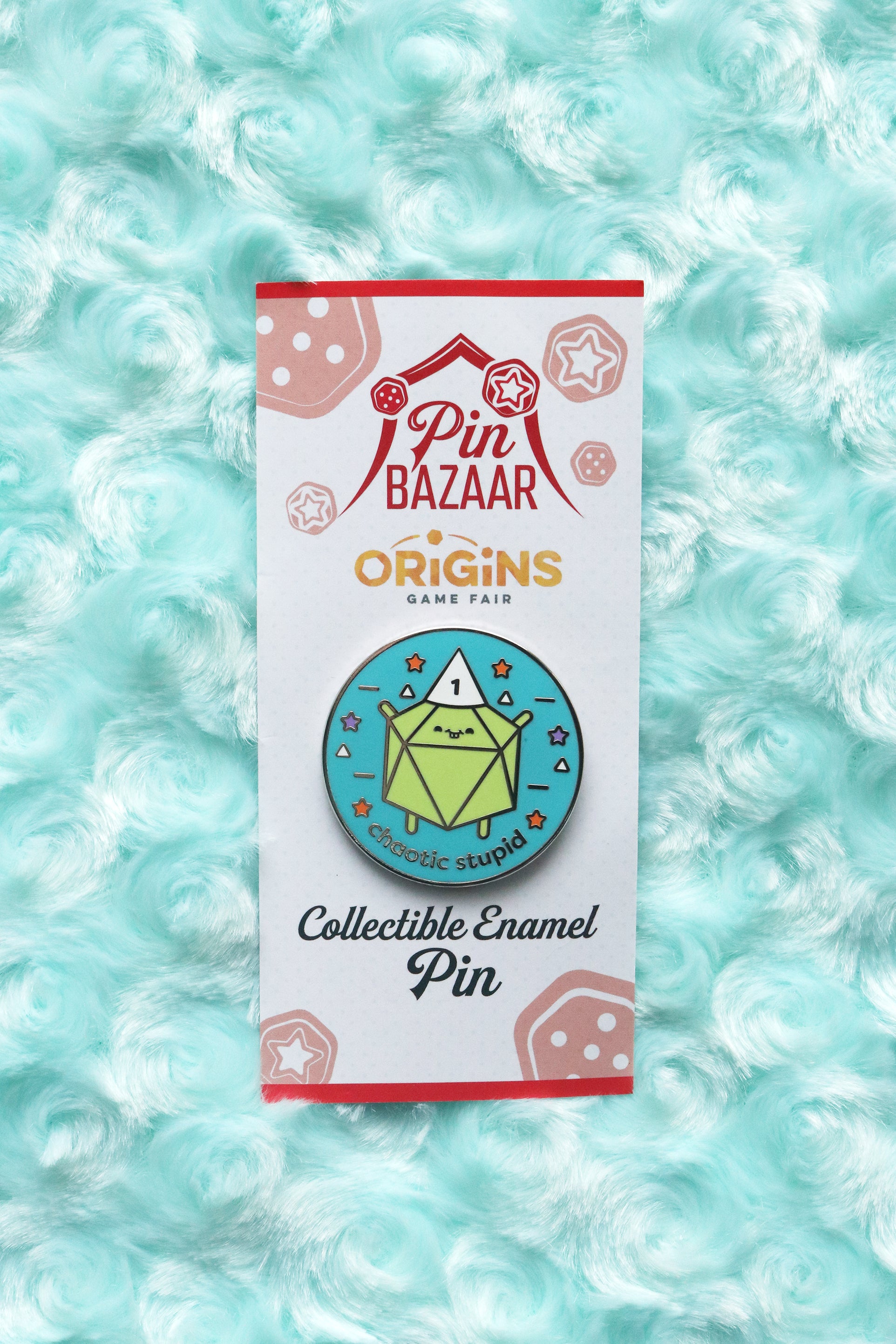 Chaotic stupid enamel pin photographed on a teal fabric background.