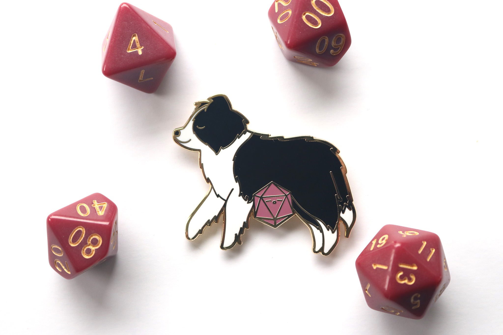Enamel pin of a sleepy black and white Border Collie with a mauve colored d20. Photographed on a white background with mauve polyhedral dice surrounding it.