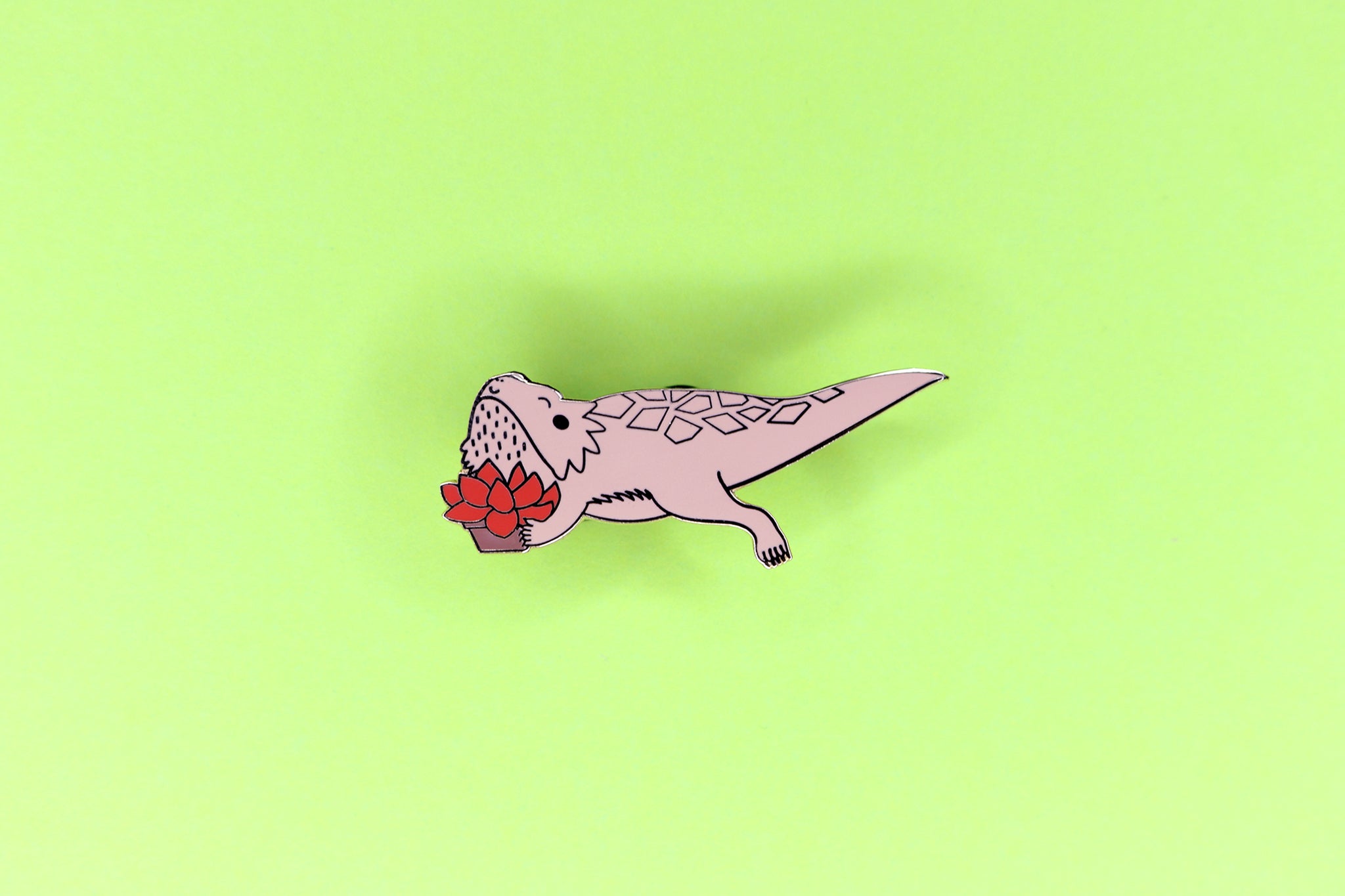 hard enamel pin of a copper bearded dragon holding a red succulent
