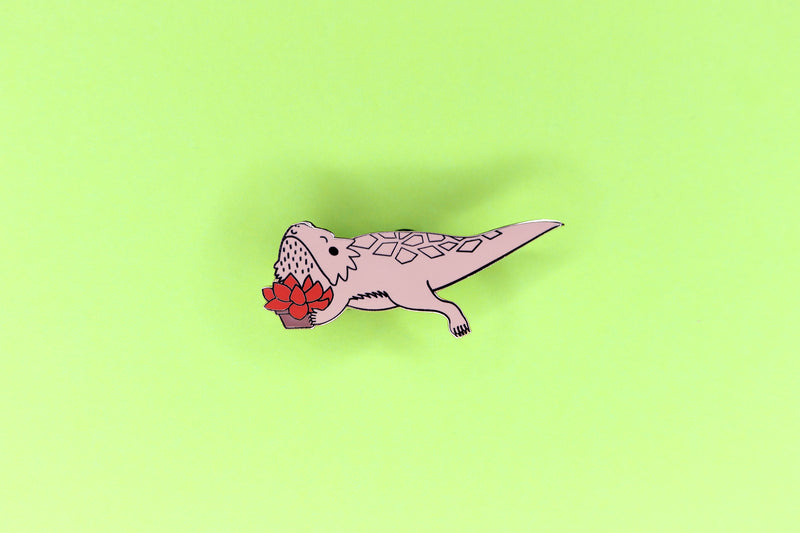 hard enamel pin of a copper bearded dragon holding a red succulent