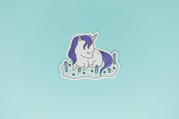Sticker of Gray and Purple Unicorn laying in field of purple flowers and blue crystals