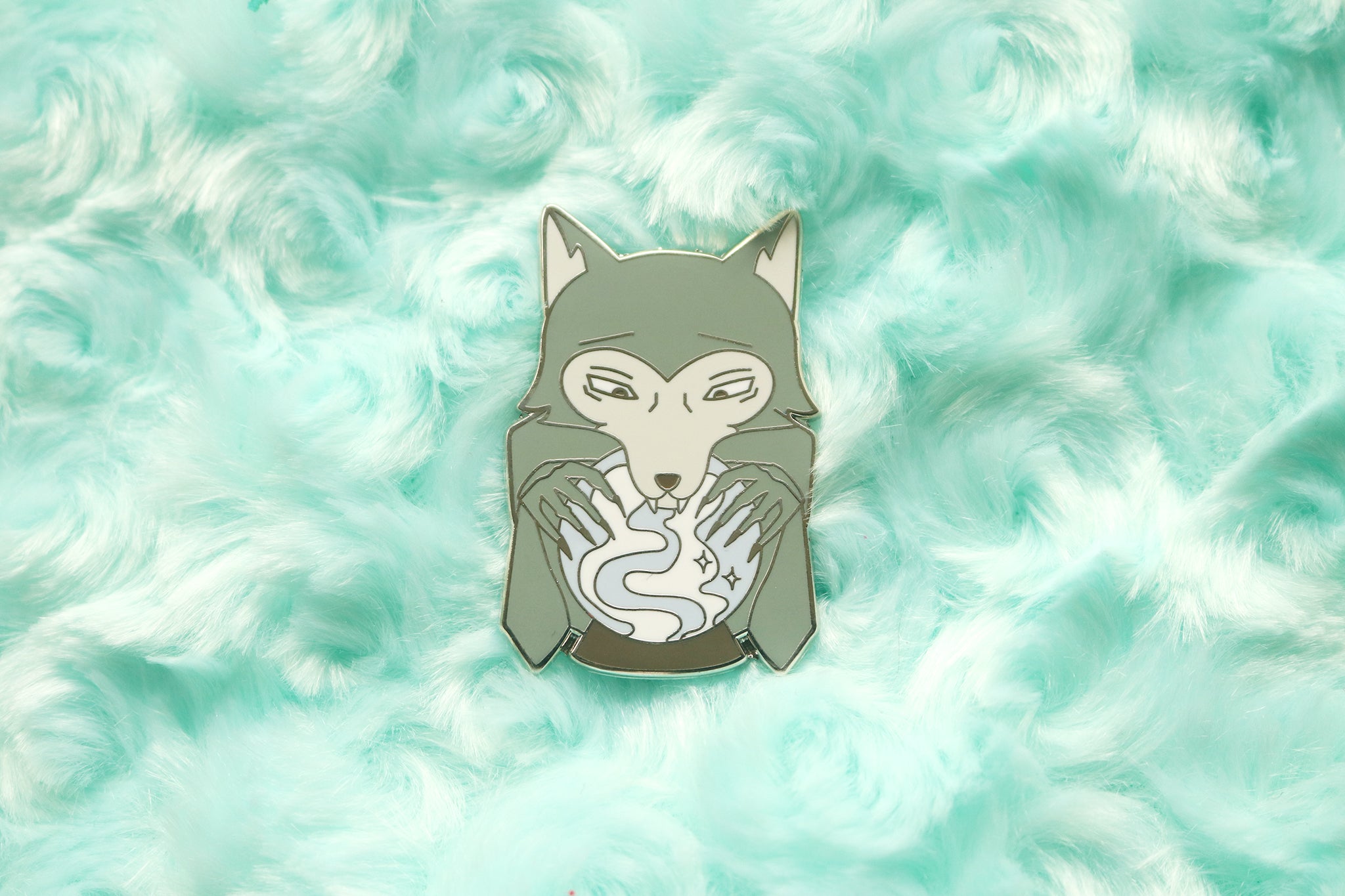 enamel pin of a grey wolf looking into a blue and white crystal ball.