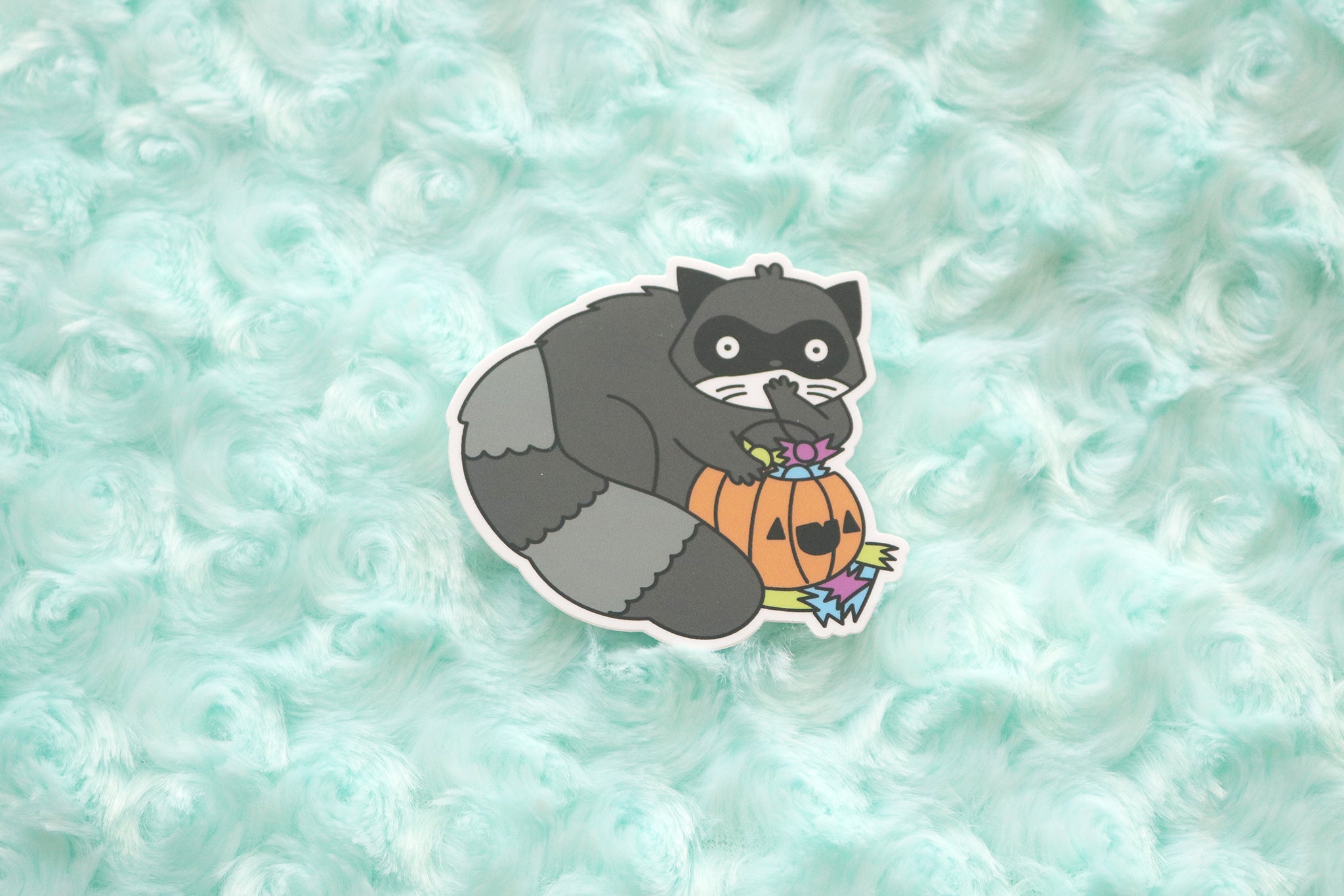 Raccoon vinyl sticker shows a shocked looking trash gobbler shoving halloween candy in his mouth straight for a trick-or-treaters candy bucket.